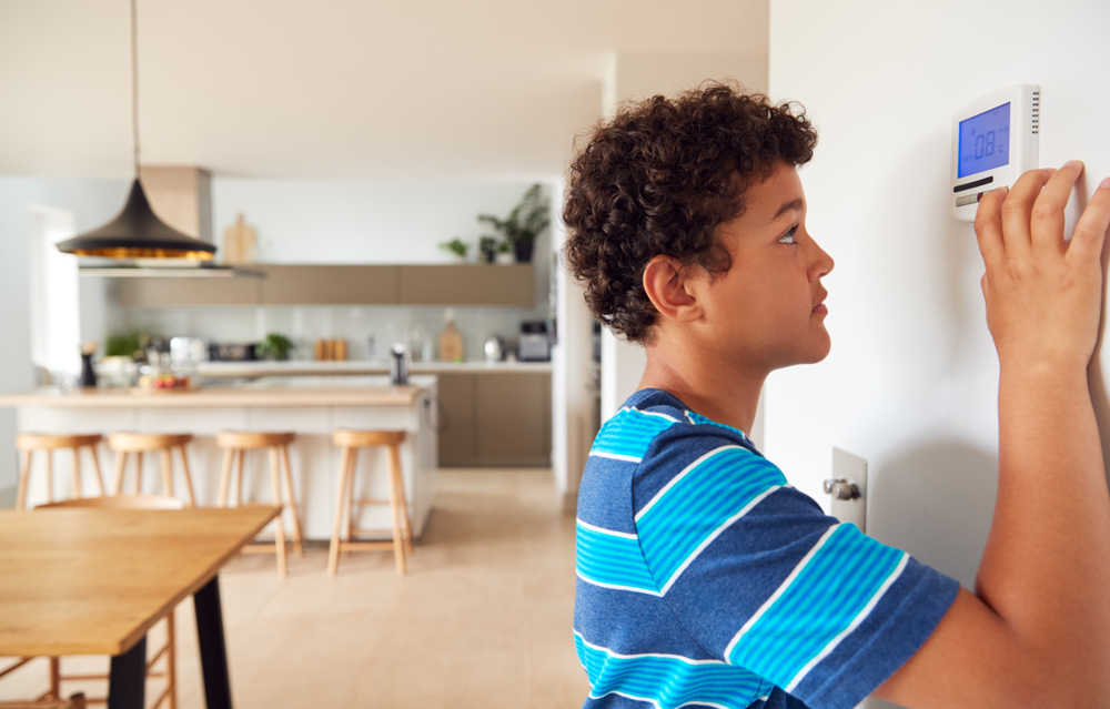 Boy Changes Temperature On Central Heating Thermostat Control Using Mobile Phone App