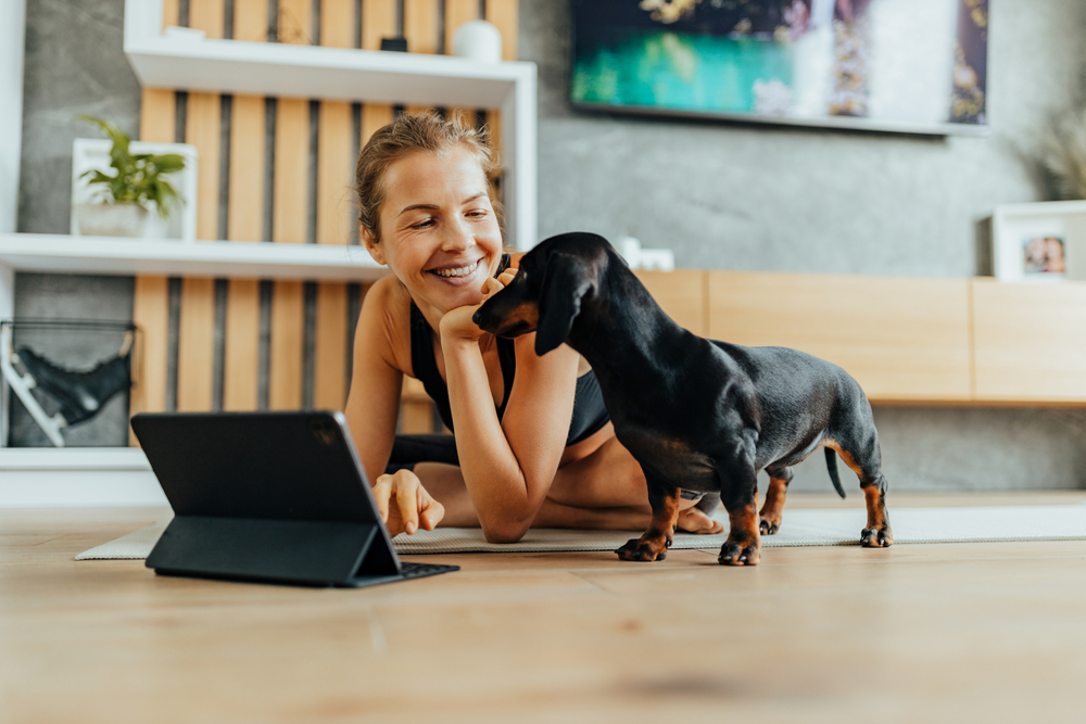 Women doing yoga on the floor next to her dog while using a laptop