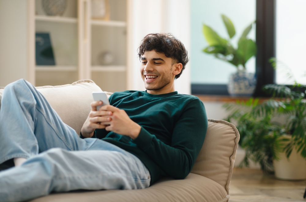 Man using phone lying on couch relaxing at home