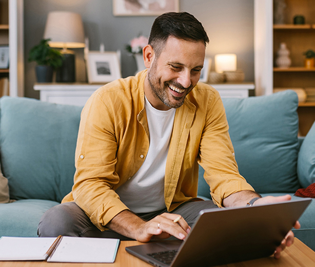 Man wearing a yellow shirt sat in lounge using a laptop