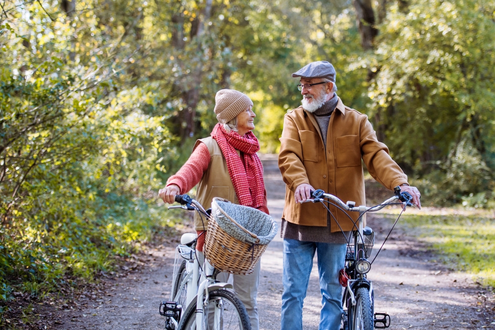 Lovely elderly couple on a walk in the forest, pushing their bikes side by side