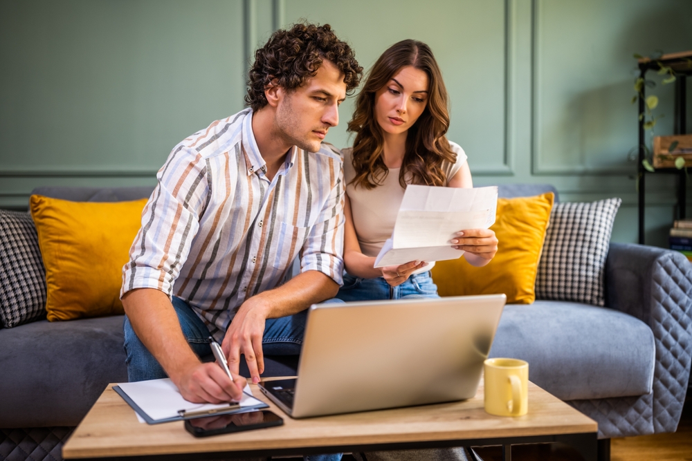 Couple sat on sofa reviewing documents and using a laptop