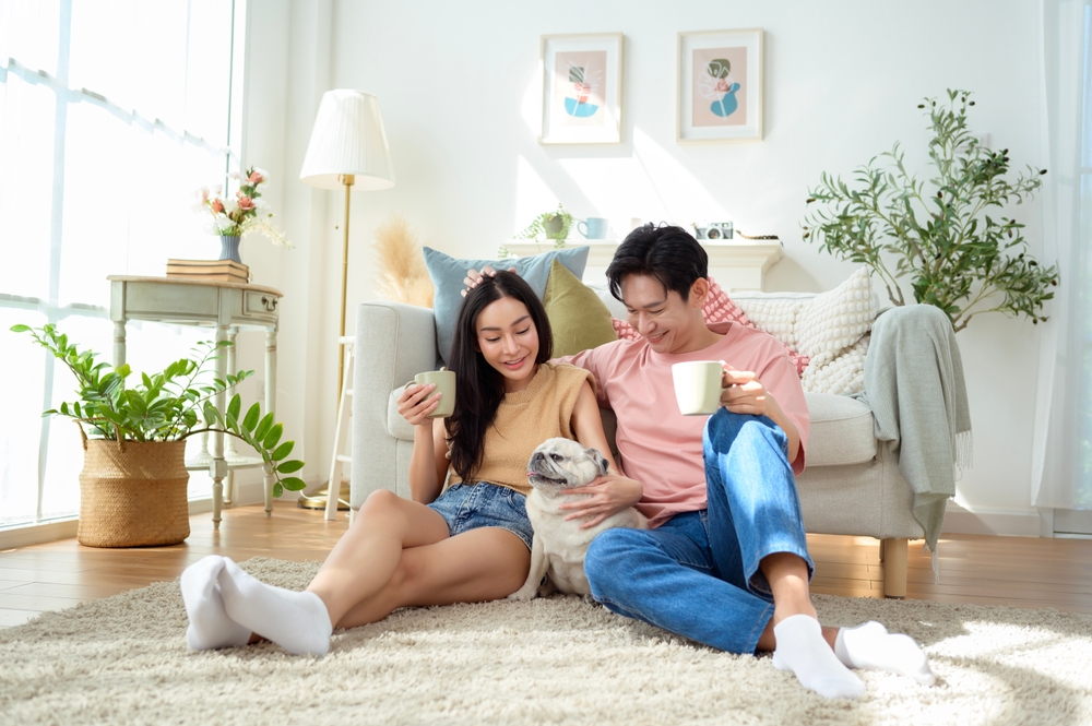 A couple relaxes on the floor with their pug, sharing a light breakfast in a sunny room.