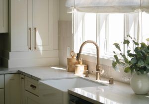 Bright modern kitchen interior with new-build incentives farmhouse apron sink and brass faucet beneath a sunlit window in a staged residential home