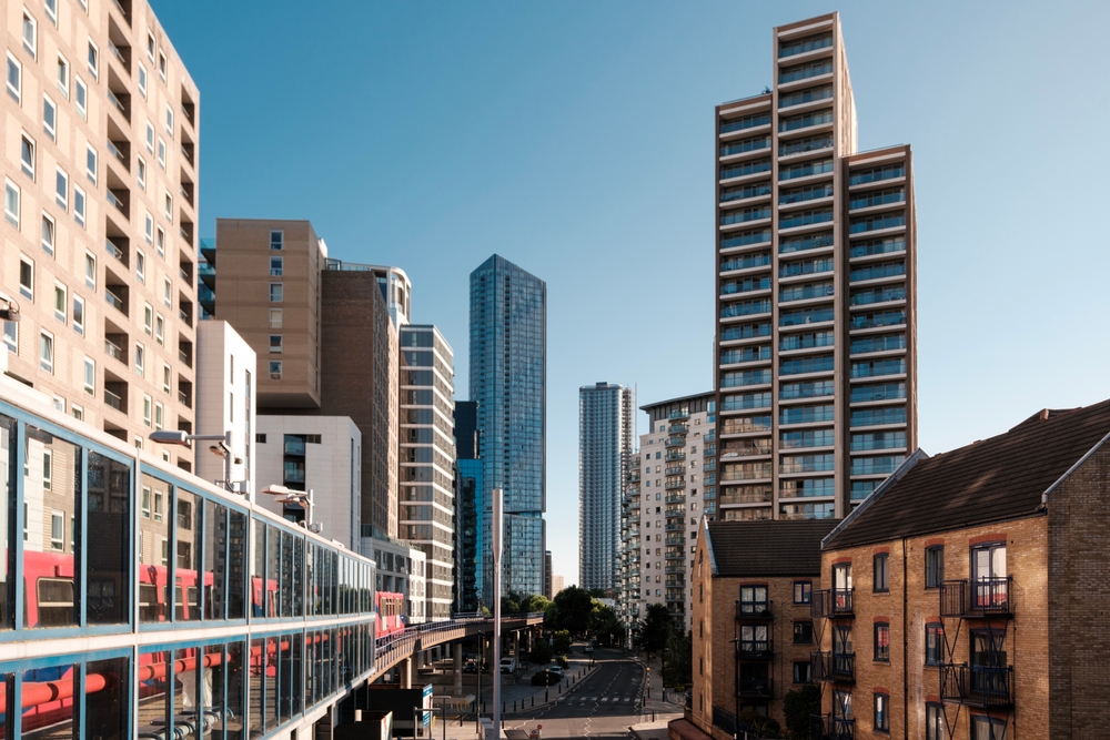 Docklands light railway (dlr) train travels through poplar, showcasing the contrast between modern high-rise buildings and traditional brick architecture under a clear blue sky